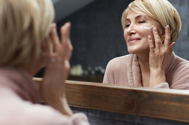 Vrouw voor de spiegel smeert creme op