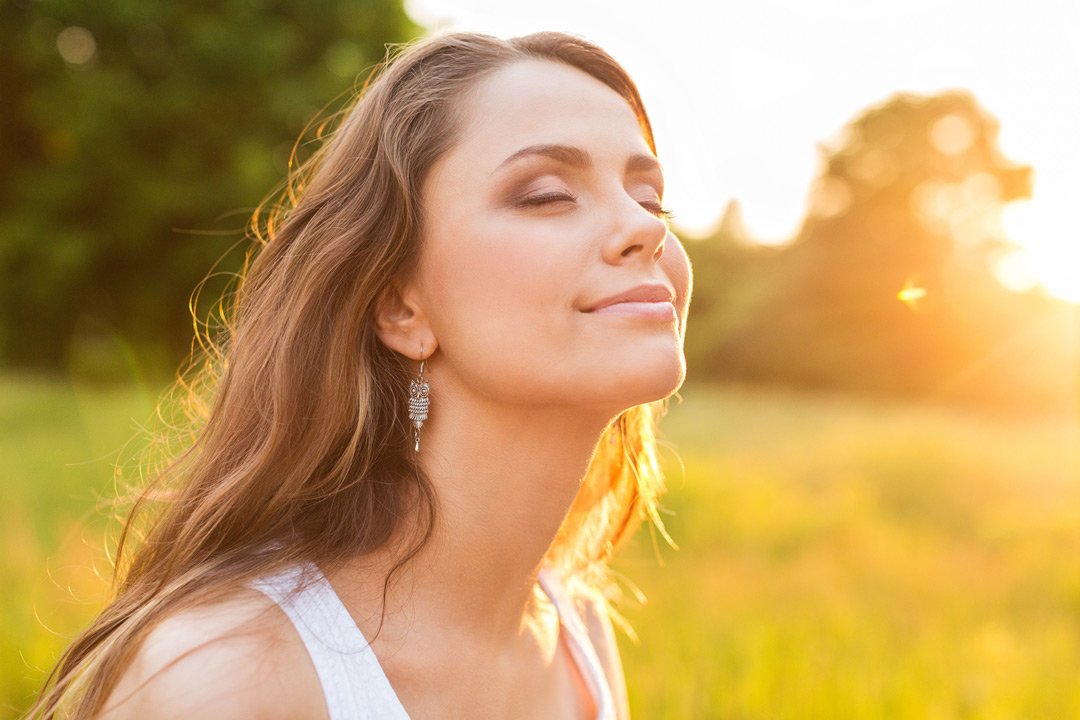 vrouw geniet van zonnestralen in een groen veld, met haar gezicht omhoog gericht naar de zon.