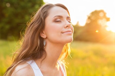 vrouw geniet van zonnestralen in een groen veld, met haar gezicht omhoog gericht naar de zon.